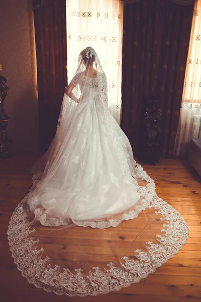 Novia en boda blanca. Hermosa novia en vestido de novia blanco de pie en su dormitorio cerca de la ventana  . — Foto de Stock