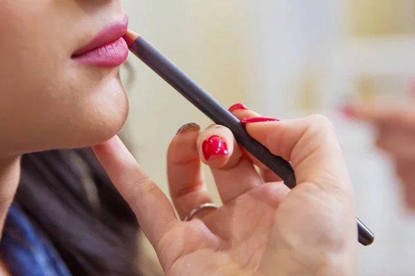 Tangan wanita dari visagiste memegang pensil dan menggambar bibir. Seniman Makeup profesional menerapkan pensil lipstik pengantin. Menutup gadis cantik tak dikenal mendapatkan bibirnya dicat . — Stok Foto