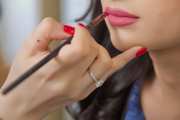 The female hand of visagiste is holding a pencil and drawing lips . Professional Makeup artist applies pencil lipstick bridal . Close up of unrecognizable pretty girl getting her lips painted.