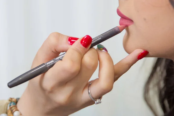The female hand of visagiste is holding a pencil and drawing lips . Professional Makeup artist applies pencil lipstick bridal . Close up of unrecognizable pretty girl getting her lips painted.