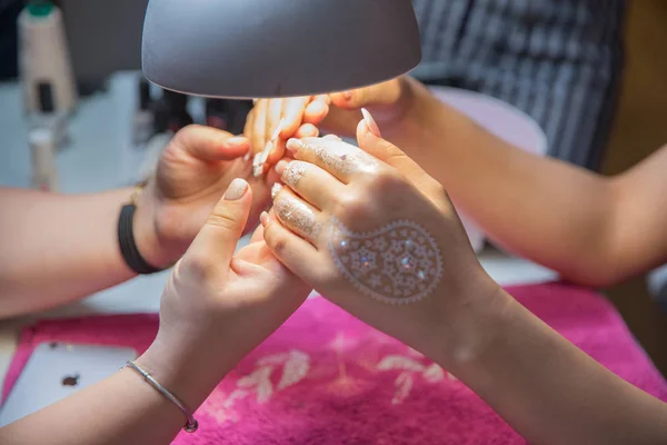 Toma su mano y mira a la luz. artista callejero dibuja patrones de henna en su mano en unas vacaciones de la ciudad. Barniz rosa en la uña. Atrae henna en sus manos  . — Foto de Stock