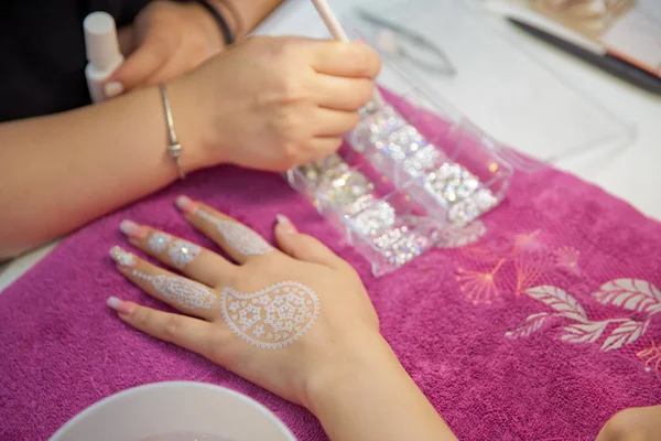 Le maître dessine sous la forme d'une plume buta sur sa main avec du gel blanc. artiste de rue dessine des motifs de henné sur sa main pendant les vacances en ville. Vernis rose sur l'ongle. Entraîne du henné dans ses mains  . — Photo