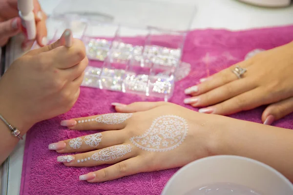 El maestro dibuja en forma de una pluma de buta en su mano con gel blanco. artista callejero dibuja patrones de henna en su mano en unas vacaciones de la ciudad. Barniz rosa en la uña. Atrae henna en sus manos  . — Foto de Stock