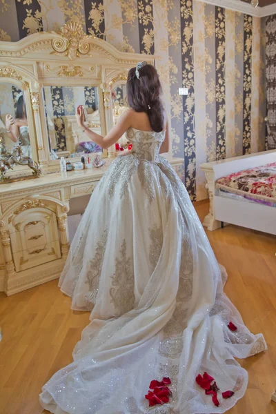 Подготовка к свадьбе. Красивая молодая невеста в белом свадебном платье в помещении. Роскошная модель, смотрящая на зеркало сидящее на стуле. Красивая невеста в зеркале в спальне  . — стоковое фото