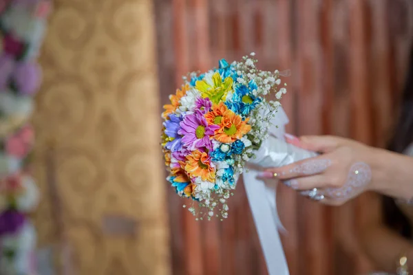 Κρατάει ένα λουλούδι του γάμου στο χέρι του. Έγχρωμη μακρο φωτογραφία ενός λεπτομερούς μπουκέτο με πολύχρωμα τριαντάφυλλα, λευκά μικρά λουλούδια και ένα ψεύτικο διαμάντι στο κέντρο του τριαντάφυλλου . — Φωτογραφία Αρχείου