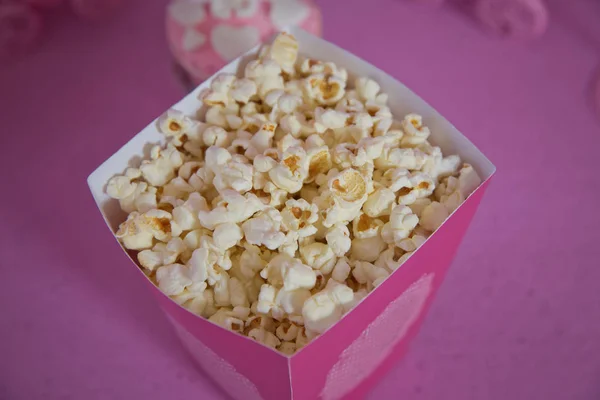 Popcorn spilled from a striped box . Three vintage-style boxes of popcorn in a carnival themed still life with arcade game pink tickets . A wide classic box of theater popcorn isolated on pink .