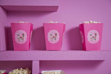 Pembe üzerine izole edilmiş geniş bir tiyatro patlamış mısırı kutusu. Azerbaycan şehrinde Lol çizgi filmleriyle bebek isimlerinin basit bir dekorasyonu. Doğum günü için dekore edilmiş lol masa. .