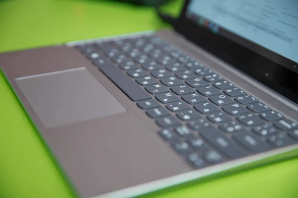 Yeşil arka planda modern dizüstü bilgisayar. Ofiste iş kavramı. Metal dizüstü bilgisayar klavye alanı küçük derinlik . Not defteri ile ofis çalışması. bilgisayarlarda saat bandına benzer metal menteşeler vardır.