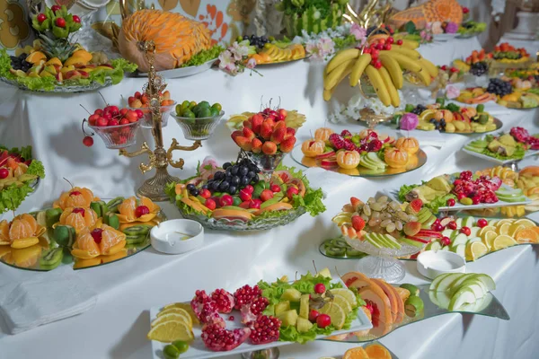 Owoce są na stole. truskawka, czarna winogrona, jabłko, pomarańcza, banan, granat, cytryna mandarynka, gruszka. posiekane owoce na białym Blat stołu — Zdjęcie stockowe