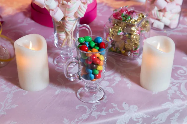 Красочные конфеты. Разноцветные конфеты. Цветные конфеты в стакане. Круглый шоколад очень красочный. Свеча  . — стоковое фото