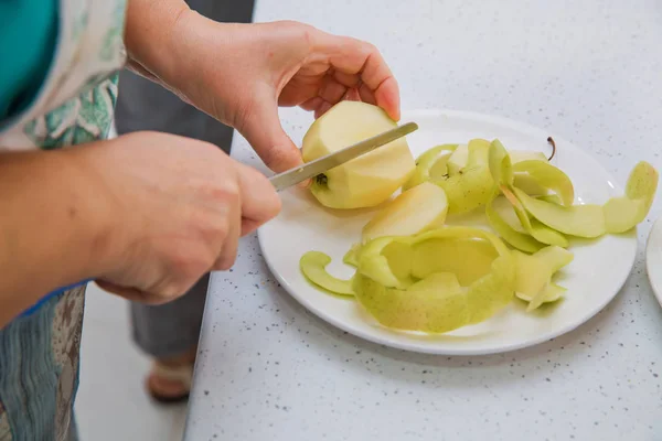 Directly above shot of Woman peeling an apple . The woman knocks on top of the apple . Female hands peeling skin off of green apple using a paring knife with bamboo plate wooden table in background .