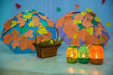 Çatıda turuncu ve sarı yapraklar var. Mum balonun içinde yanıyor. Balonun üstünde bir yaprak var. Sepette yapraklar ve meyveler var. Sonbahar dekoru.