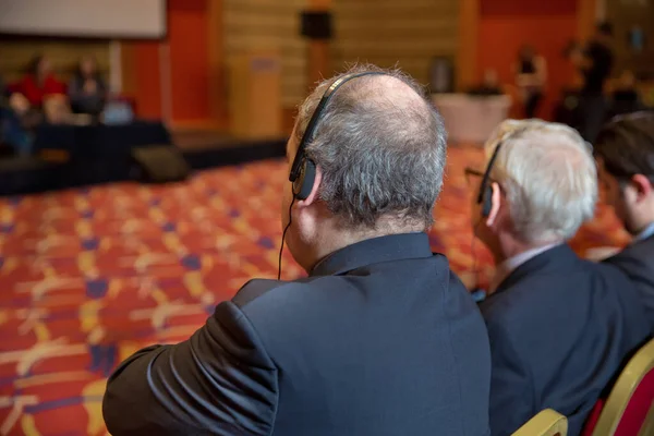 Geschäftsleute, die während der Veranstaltung über Kopfhörer übersetzen, sind nicht wiederzuerkennen. Glatzköpfiger Sicherheitsmann mit Headset zur Personenkontrolle. Hitzige Debatte auf einer Konferenz — Stockfoto