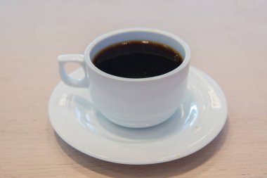 Beyaz fincan, beyaz soslu kahve. Kafe bulanık arka planda bir fincan sıcak kahve. Beyaz porselen fincanda kahve çekirdekleri ve yabani otlar. .