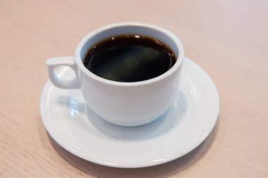 Beyaz fincan, beyaz soslu kahve. Kafe bulanık arka planda bir fincan sıcak kahve. Beyaz porselen fincanda kahve çekirdekleri ve yabani otlar. .