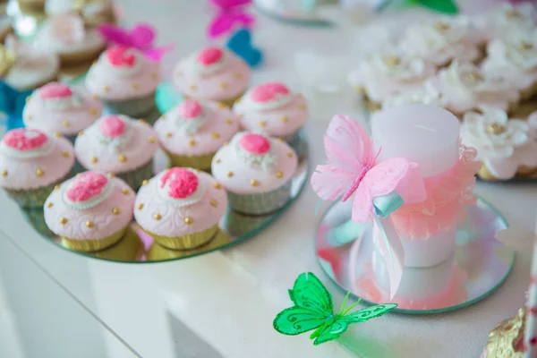Kuchen im Hintergrund. künstlicher rosa und grüner Schmetterling auf weißer Kerze. — Stockfoto