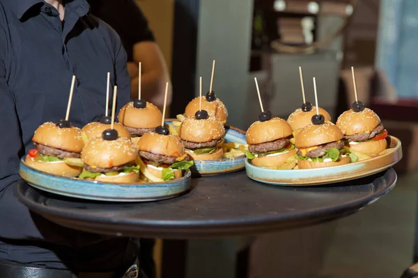Waiter carrying a tray of appetizers. Outdoor party with finger food, burgers, sliders. man hold tray with burger at restaurant. Mens hands hold a tray with a cheeseburger. Catering service.