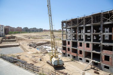 Yeni bina, kule vincinin kullanımıyla inşa ediliyor. İnşaat alanında açık mavi gökyüzü ile çalışan birkaç vinç de dahil olmak üzere büyük inşaat alanı.