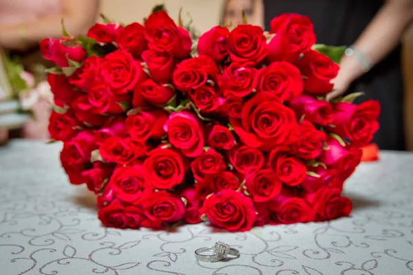 Glass table . Wedding rings next to a red flower bouquet selective focuse . Bride and groom with Engagement gold rings put on the table, and next to them lies a wedding bouquet . — Stock Photo, Image