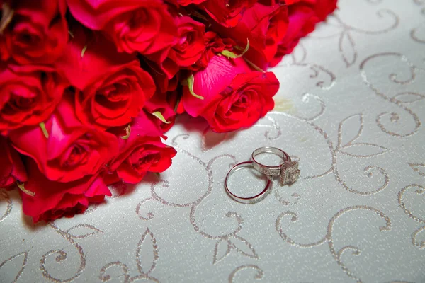 Mesa de cristal. Anillos de boda junto a un ramo de flores rojas enfoque selectivo. Novia y novio con anillos de oro Compromiso poner sobre la mesa, y al lado de ellos se encuentra un ramo de bodas . — Foto de Stock