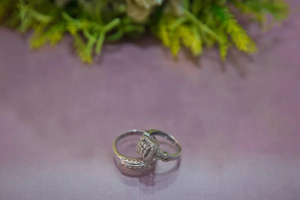 Noiva e noivo com anéis de ouro de noivado colocados sobre a mesa, e ao lado deles está um buquê de casamento. Anéis de noivado. Anéis de casamento ao lado de um buquê de flores brancas focuse seletivo  . — Fotografia de Stock