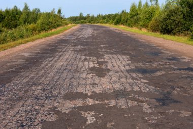 Güneşli yaz günde ağaçlarıyla çevrili boş asfalt köy yolunda kırık.