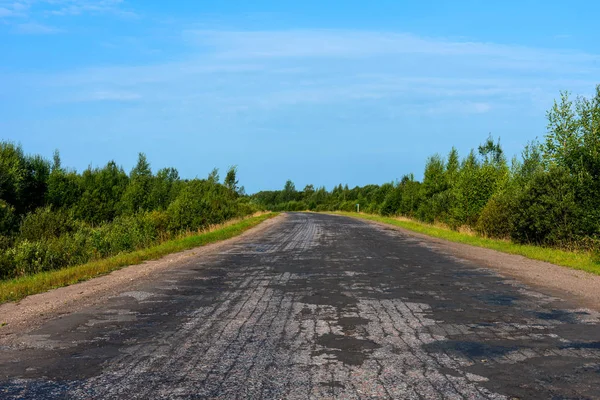 Güneşli yaz günde ağaçlarıyla çevrili boş asfalt köy yolunda kırık.
