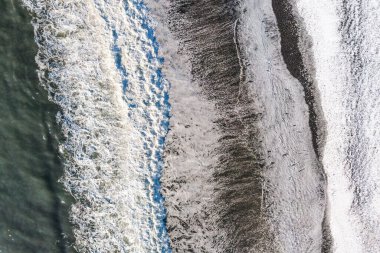 İzlanda 'da Reynisfjara dalgalı siyah kumsal manzarası. Reynisfjara 'nın insansız hava aracındaki kış manzarası. Kışın kar altında siyah kumsal.