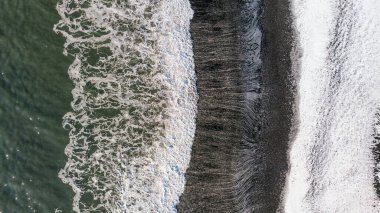 Amazing picturesque view of black sand beach with wave of Reynisfjara in Iceland. Aereal winter landscape view of Reynisfjara from drone. Black sand beach under snow at winter time. clipart
