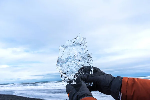 在冰岛 一只手拿着冬季手套的雄性手拿着一块冰川 在冰岛Jokulsarlon泻湖附近的钻石海滩上 一只雄性手拿着一大块冰 — 图库照片
