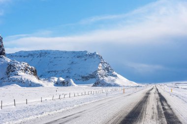 İzlanda 'da kışın karlı arazinin arka planında boş asfalt yol. Karlı ve mavi gökyüzü olan İzlanda karayolu..