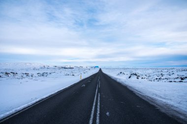 Kışın İzlanda 'da kar manzarasının arka planında boş asfalt yol. Karlı ve mavi gökyüzü İzlanda 'da.