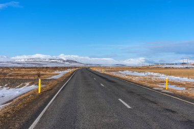 Kışın İzlanda 'da kar manzarasının arka planında boş asfalt yol. Güneşli bir günde İzlanda 'ya giden otoyol..