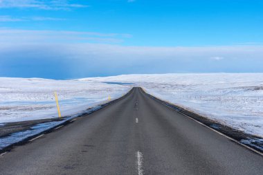 Kışın İzlanda 'da kar manzarasının arka planında boş asfalt yol. Güneşli bir günde İzlanda 'ya giden otoyol..