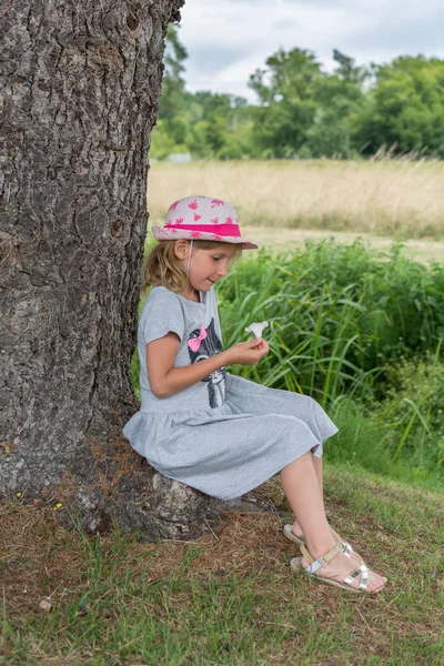 Küçük kız yaşlı ağacın altında oturup beyaz çiçekli