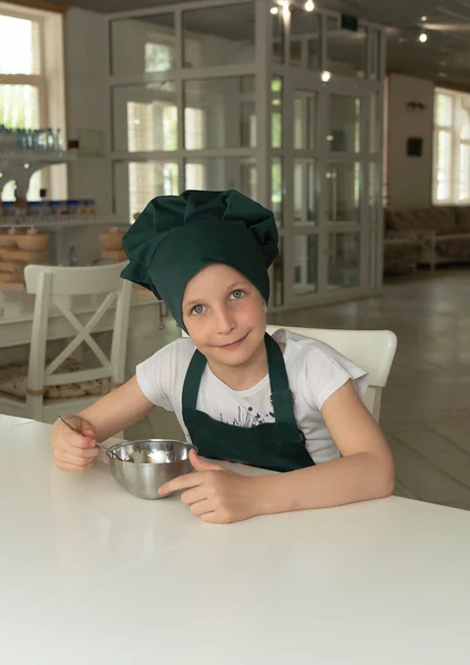 Beautiful young cook chef girl in green chef cap with a spoon and a bowl
