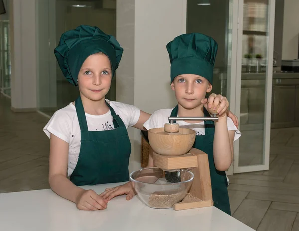 Couple of young cook chef girls in green chef caps with manual kitchen mill