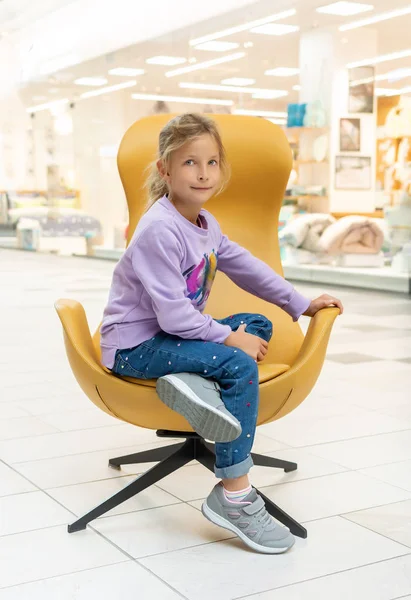 Mała dziewczynka w niebieskim skoczkiem siedzi w żółtym krześle — Zdjęcie stockowe