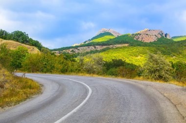 Tepeler arasında yol ağaçlar ve çalılar ile kaplı. Parlak güneşli bir günde.