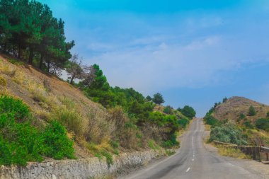 Düz yol tepeler arasında gidiyor ağaçlar ve çalılar ile kaplı. Parlak güneşli bir günde.