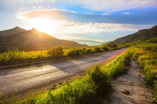 Sunset in cloudy sky over mountains and road — Stock Photo, Image