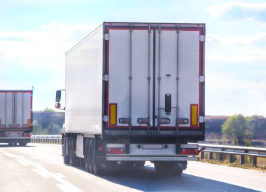 Parlak güneşli bir günde yarı karavanlı kamyonlar köy yolunda ilerler. Arka plan.