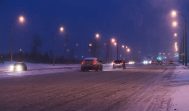 Arabalar kışın gece karla kaplı yol boyunca yol alırlar..