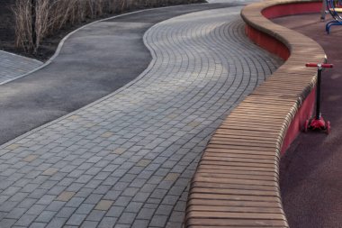 Oyun parkında uzun ahşap bir bank olan dolambaçlı kaldırım.