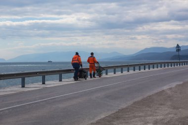 İş kıyafetleri içinde yol işçileri kıyı boyunca otoyol boyunca gidiyor.