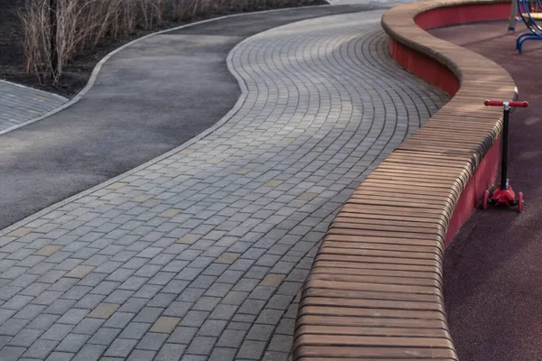 Oyun parkında uzun ahşap bir bank olan dolambaçlı kaldırım.