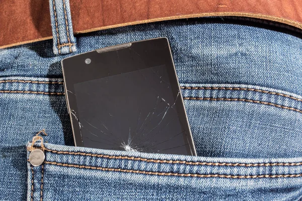 Smartphone with a broken screen in the back pocket of jeans. Close-up