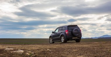 Bulutlu bir gökyüzü altında sahada SUV. 