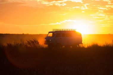 Minivan gün batımında bir köy yolunda gidiyor.
