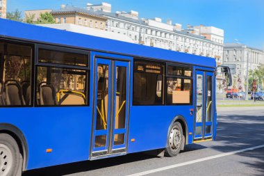 Mavi normal otobüs şehirde caddeden aşağı doğru ilerliyor.